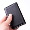 A hand holds a black stitched PU leather card holder wallet.