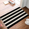A rectangular black and white striped non-slip door mat placed on a wooden floor.