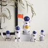 A collection of handcrafted astronaut figurines in white and blue resin, including one with an orange flag.