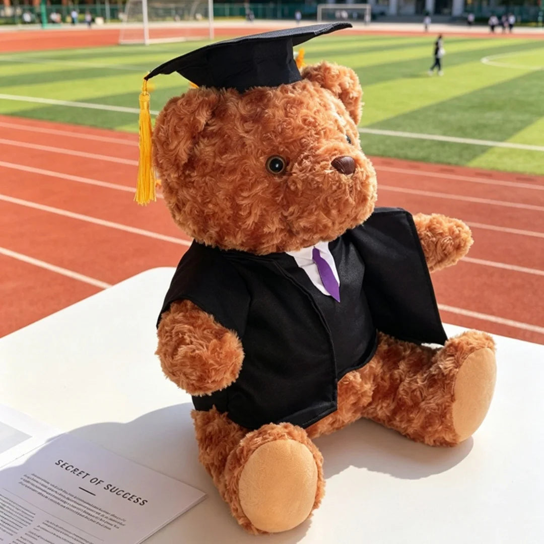 Jouet en peluche brun d'un docteur portant une robe de graduation noire et une cravate violette, assis sur une surface blanch