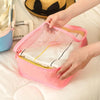 A hand is opening a pink mesh packing cube organizer filled with folded white clothing on a white surface.