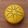 A yellow mini steel tongue drum with six tuning holes marked 1 through 6 rests on a wooden surface.