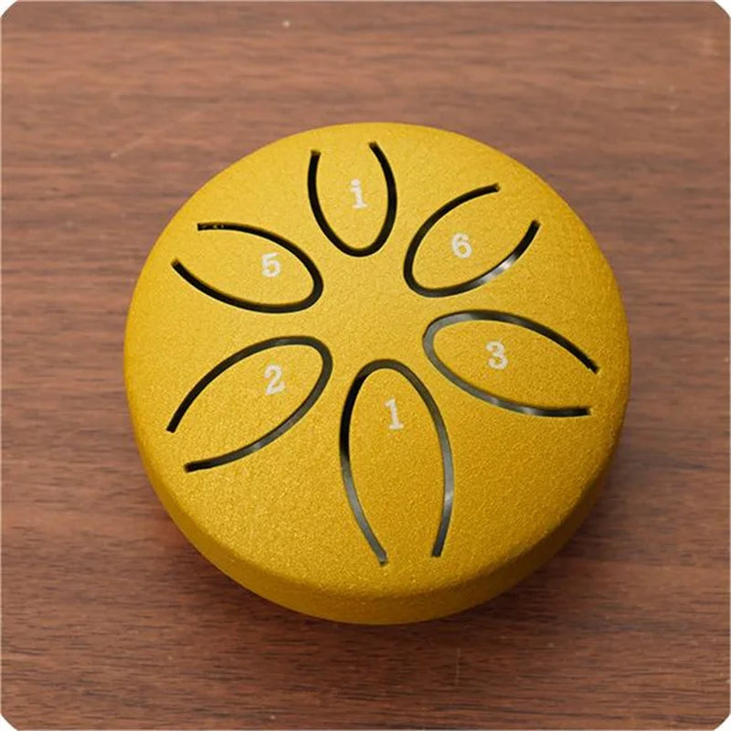 A yellow mini steel tongue drum with six tuning holes marked 1 through 6 rests on a wooden surface.