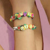 A wrist is adorned with a bracelet made of assorted polymer clay beads shaped like summer fruits.