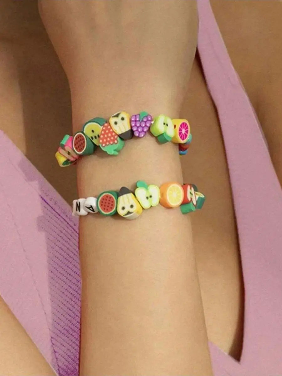 A wrist is adorned with a bracelet made of assorted polymer clay beads shaped like summer fruits.