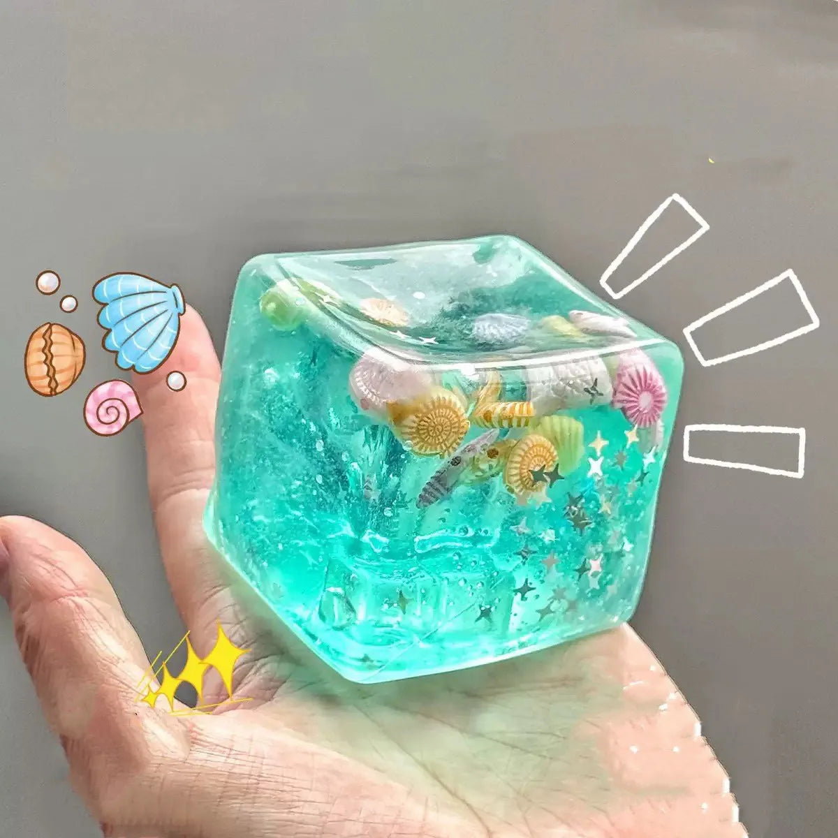 A hand holds a translucent teal ocean squishy stress ball filled with colorful sea creatures and glitter.