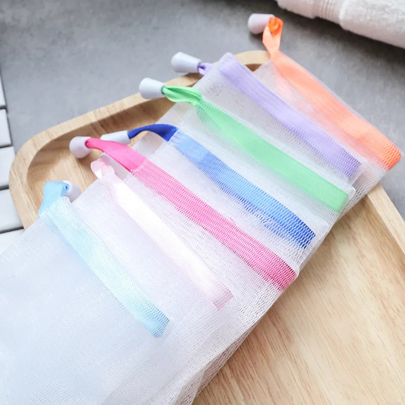 A set of foaming mesh bath poufs with colorful hanging loops displayed on a wooden tray.