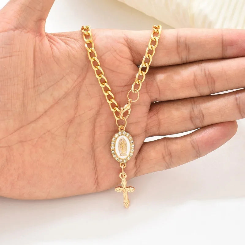 A gold chain necklace with an oval pendant featuring a cross hanging, held in a person's hand.