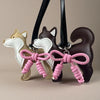 A brown and white Shiba Inu PU leather bag charm with a pink braided bow hanging from a black strap.