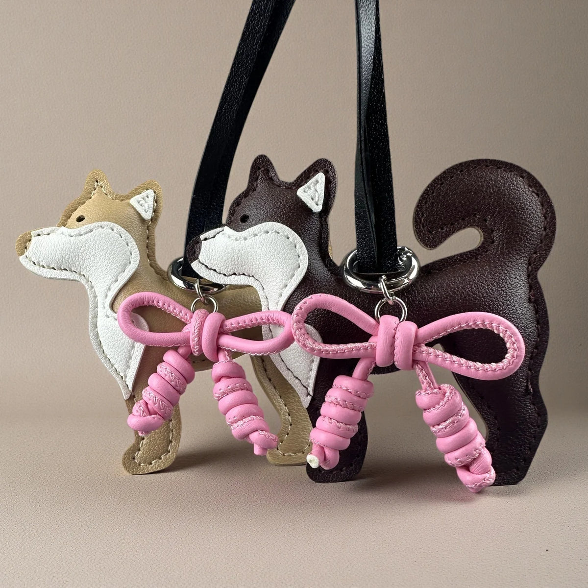 A brown and white Shiba Inu PU leather bag charm with a pink braided bow hanging from a black strap.