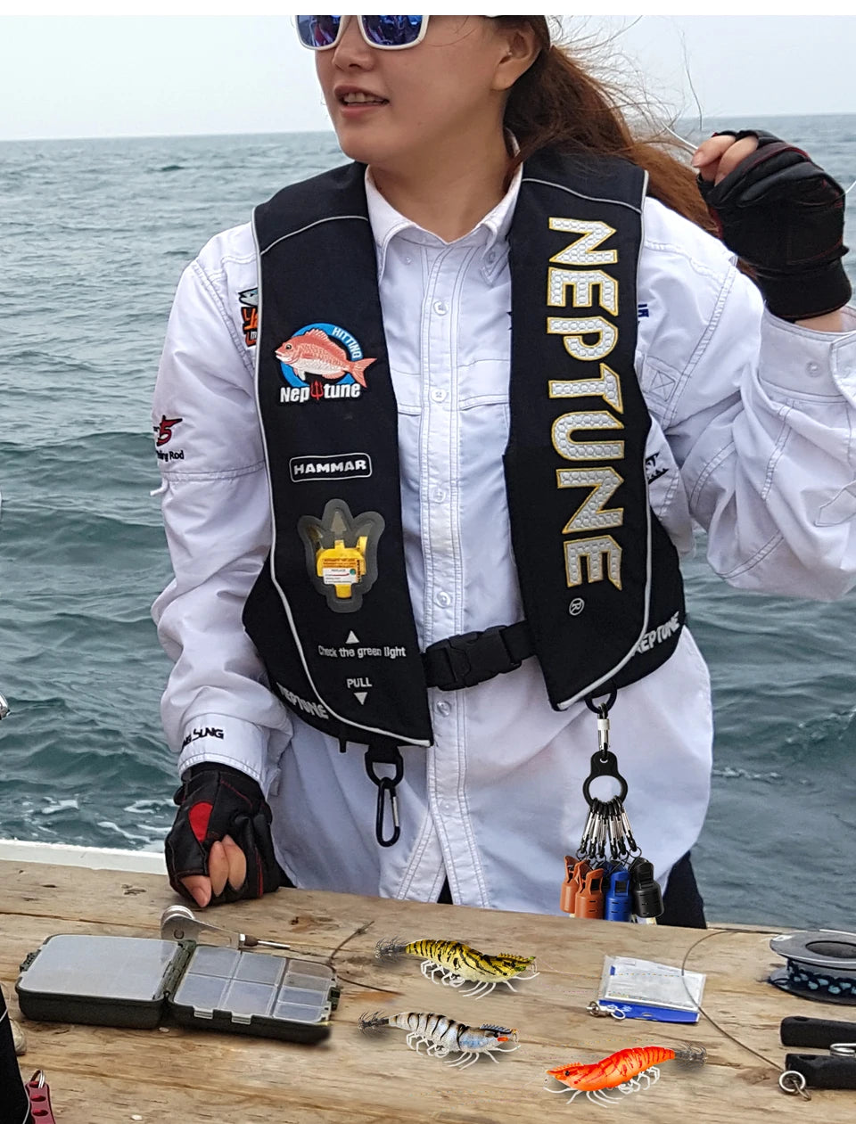 A person wearing a white shirt and black vest holds a squid jig protector kit with carabiner on a wooden surface.