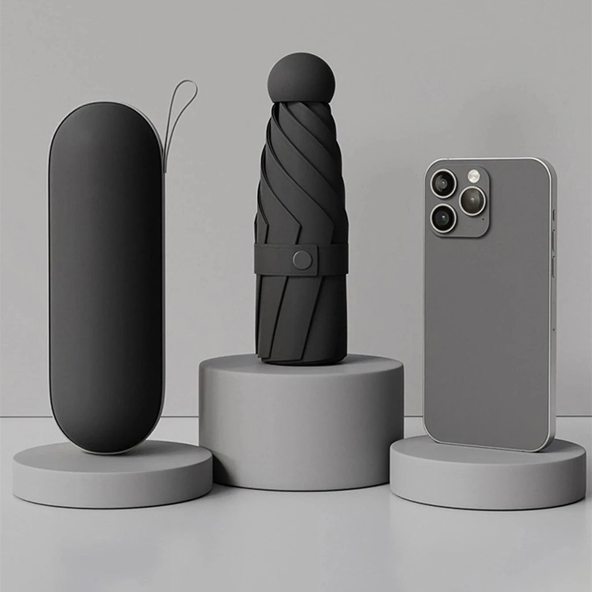 A compact folding umbrella in a dark gray color is displayed next to a smartphone.