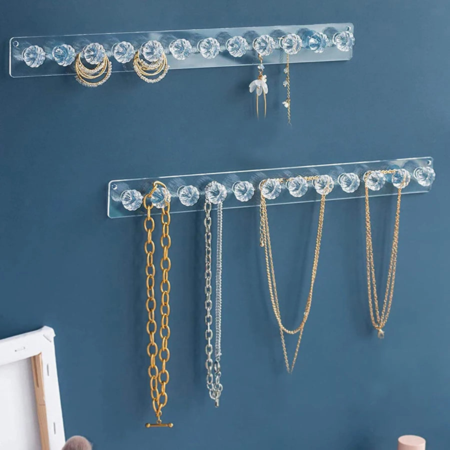 Wall-mounted acrylic jewelry organizer displaying various necklaces and earrings on a blue wall.