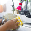 A hand is wiping a stainless steel plate with a yellow plaid kitchen towel in a kitchen setting.