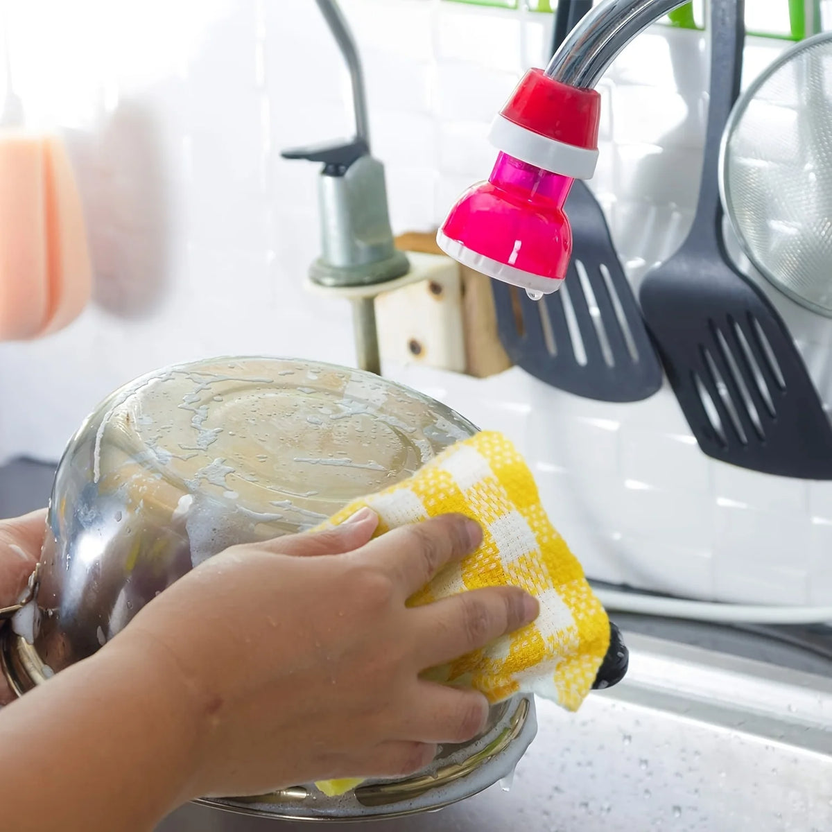 A hand is wiping a stainless steel plate with a yellow plaid kitchen towel in a kitchen setting.