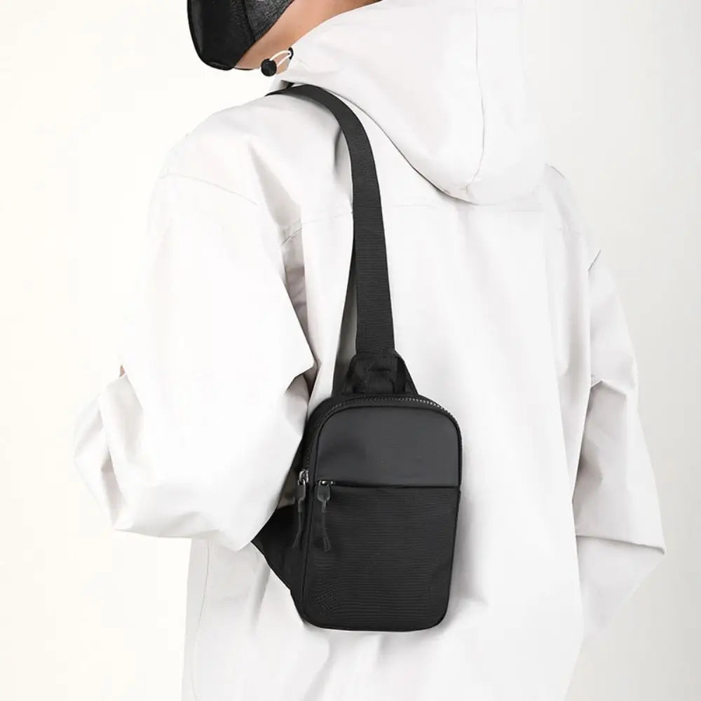 A black compact canvas crossbody sling bag worn on a white hoodie.