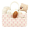 A beige floral diaper organizer bag with multiple compartments and a teddy bear toy.