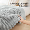 A hand is touching a soft gray brushed flannel throw blanket on a bed, enjoying coziness and leisure.