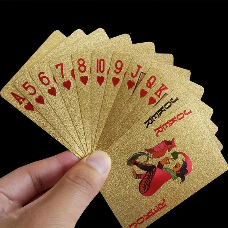 A hand holds a deck of luxury gold foil playing cards showing the Ace through King in red hearts.