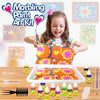 A smiling girl holds an open Marbling Paint Art Kit with colorful fluid art supplies and paint on a wooden table.