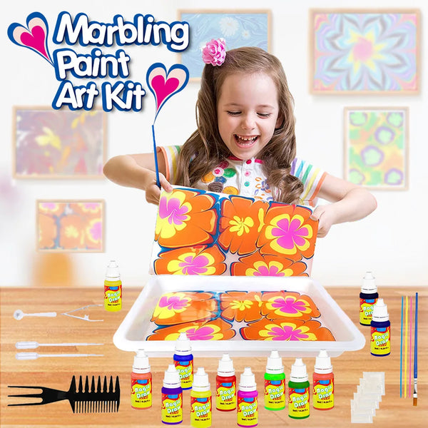 A smiling girl holds an open Marbling Paint Art Kit with colorful fluid art supplies and paint on a wooden table.