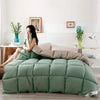 A large, quilted sage green comforter is displayed on a bed in a bright room.