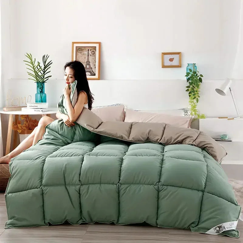 A large, quilted sage green comforter is displayed on a bed in a bright room.