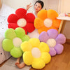 A plush sunflower pillow with soft orange, yellow, and purple petals is displayed on a wooden floor.