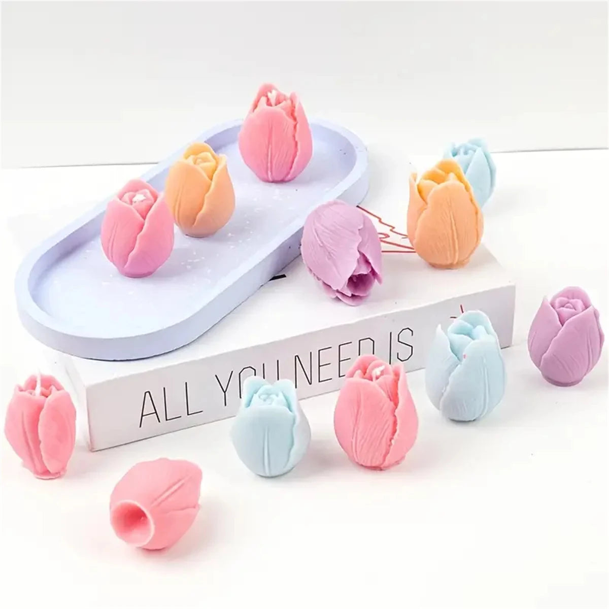 A collection of pink, peach, and blue 3D tulip silicone molds for candle and soap making displayed on a white surface.