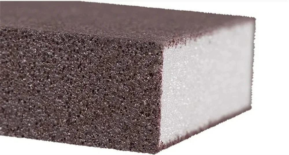 A rectangular block of dark gray Emery cleaning sponge with a white foam core.