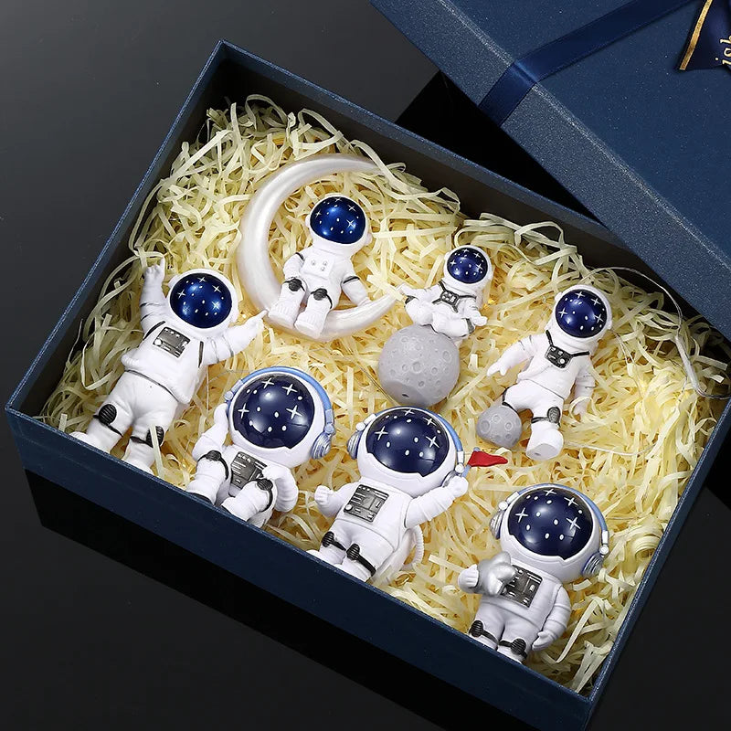 A collection of handcrafted astronaut figurine resin spacemen and a ring displayed in a dark blue box.