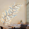 A decorative branch lamp shaped like a cherry blossom tree with blue LED lights mounted on a wall.