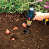 A hand uses a garden auger tool to drill a hole in dark soil, showing a root or tuber.