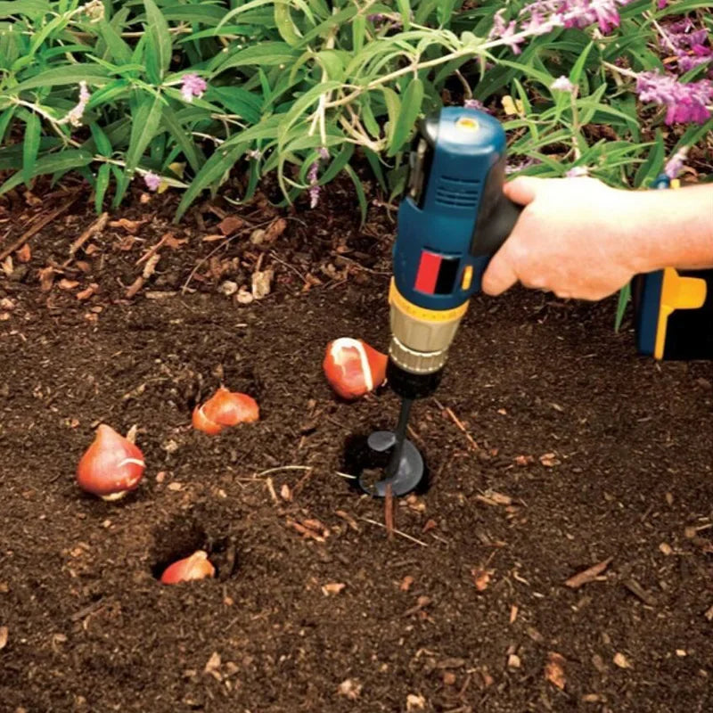 A hand uses a garden auger tool to drill a hole in dark soil, showing a root or tuber.