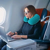 A woman works on a laptop in an airplane seat using a self-inflating travel neck pillow.