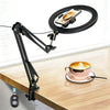 A black adjustable phone stand with an overhead light is positioned above a wooden table, illuminating a cup of coffee.