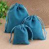 Two teal velvet drawstring jewelry pouches resting on a beige woven surface.
