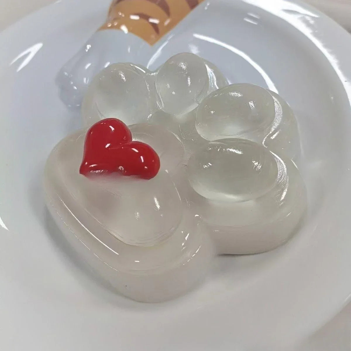 A white silicone squeeze toy shaped like a cat paw with a red heart detail is displayed on a white plate.
