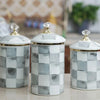 Three white and gray checkerboard porcelain storage jars with gold lids on a light surface.