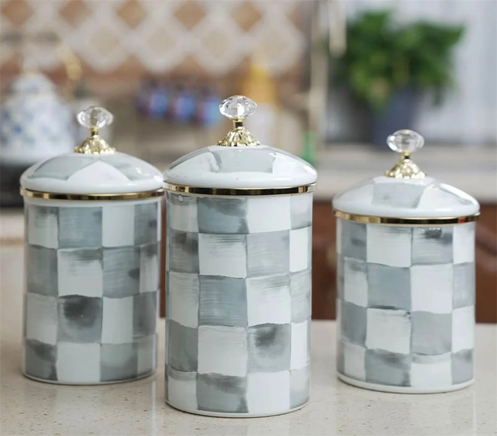 Three white and gray checkerboard porcelain storage jars with gold lids on a light surface.