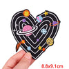 A black heart shaped embroidery patch featuring colorful planets and stars.