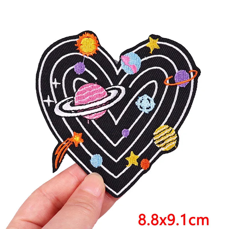 A black heart shaped embroidery patch featuring colorful planets and stars.