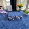 A blue plush interlocking floor mat with a striped edge is placed on a larger blue rug near a window with flowers.