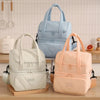 A light blue insulated reusable lunch bag is displayed next to a cream-colored one on a wooden surface.