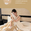 A beige plush jacquard throw blanket is draped over a bed, featuring white floral patterns.