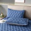 A quilted blue pillow protector resting on a bed with a matching pillow.