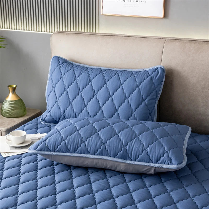 A quilted blue pillow protector resting on a bed with a matching pillow.