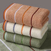 A stack of three striped bath towels in shades of brown, beige, and green resting on a green towel.