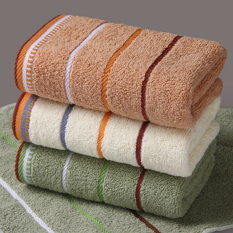 A stack of three striped bath towels in shades of brown, beige, and green resting on a green towel.