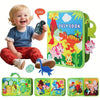 A toddler is smiling while holding a green felt busy book and several related activity boards.